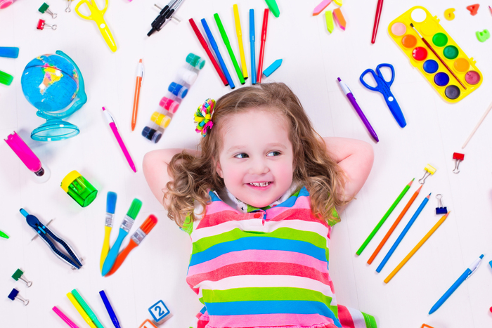 little preschool girl in stripped top lying on a white floor surrounded by stationary and school supplies 