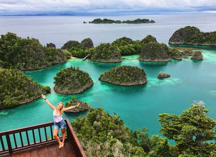 raja ampat indonesia woman standing on the edge of a wooden terrace overlooking the ocean with a lot of small islands