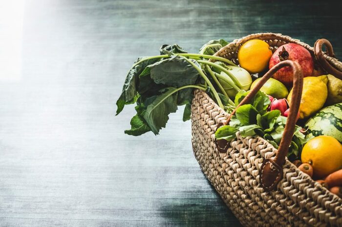 seasonal veggies in a woven basket on the floor pomegranates lemons raddish and other furits and veggies