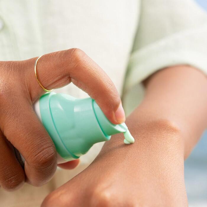 woman hands applying a small amount of sunscreen from a mint green bottle on the back of her hand