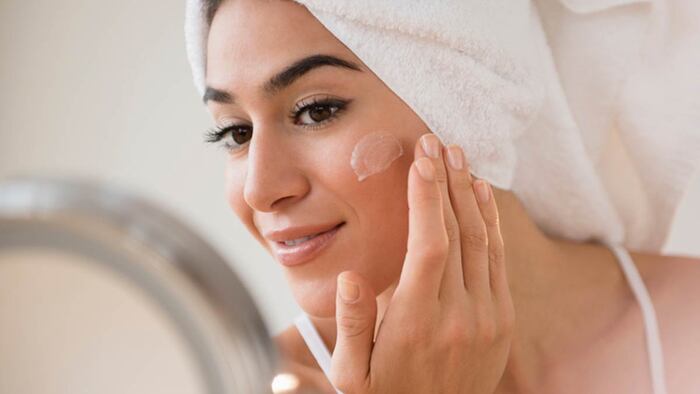 sunscreen indoors woman with a towel on her hair with dark eyes and eyebrows applying sunscreen on her face