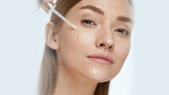 woman with light brown hair and light eyes applying serum on her face with a little drop 