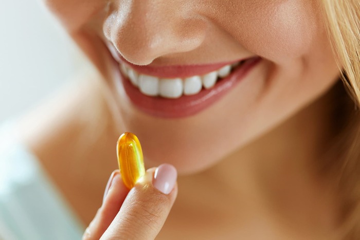 blond woman smiling and bringing a yellow capsule pill antioxidant supplement to her mouth