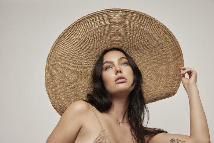 woman with a dark hair and blue eyes with a wide brimmed stray summer hat posing for the camera