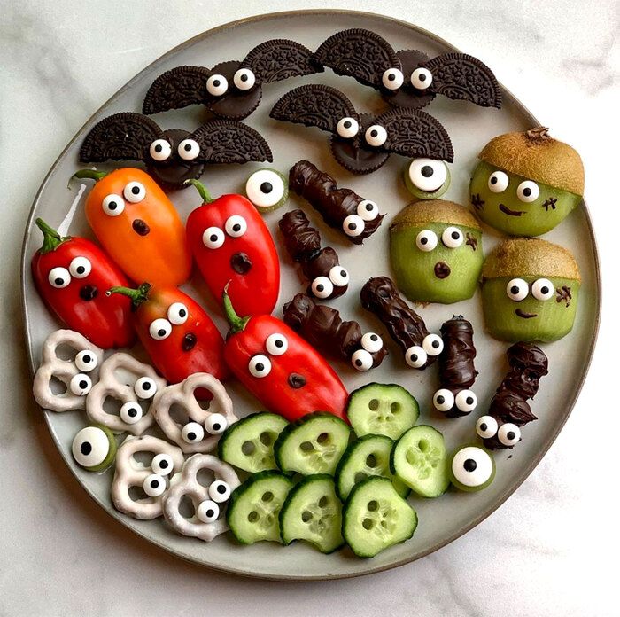 Halloween dish with a variety of halloween veggie snacks ghosts kiwis red peppers cucumber slices and oreo bats