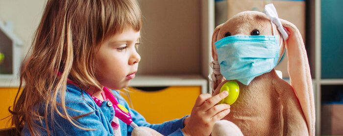 little blond baby girl playing a doctor with her soft toy bunny with a mask