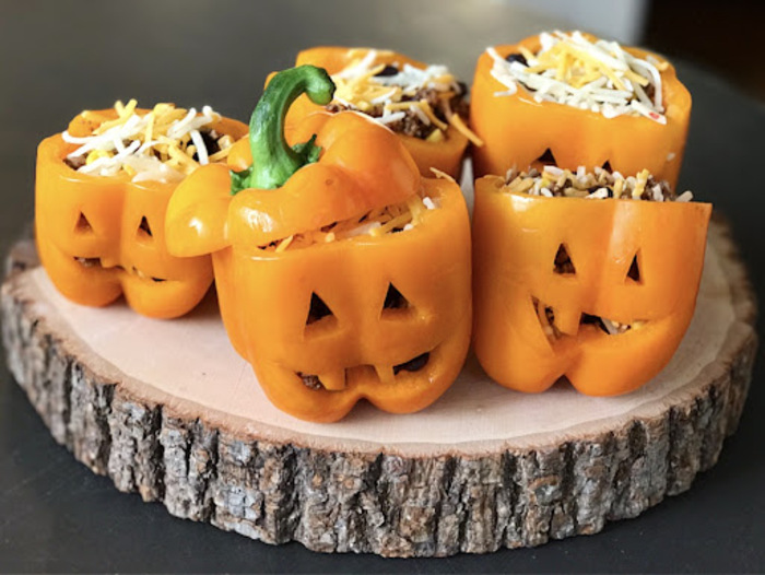 stuffed yellow halloween bell peppers on a wooden piece with carved faces and grated cheese on top