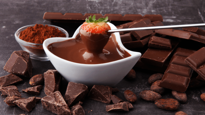 chocolate fondue in a small white bowl with a strawberry surrounded by scattered chocolate and cocoa nibs
