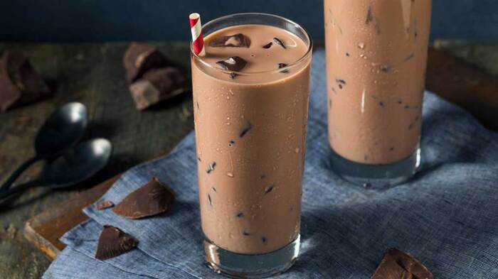 chocolate milk in tall glasses with ice cubes and red and white straws on a blue piece of cloth