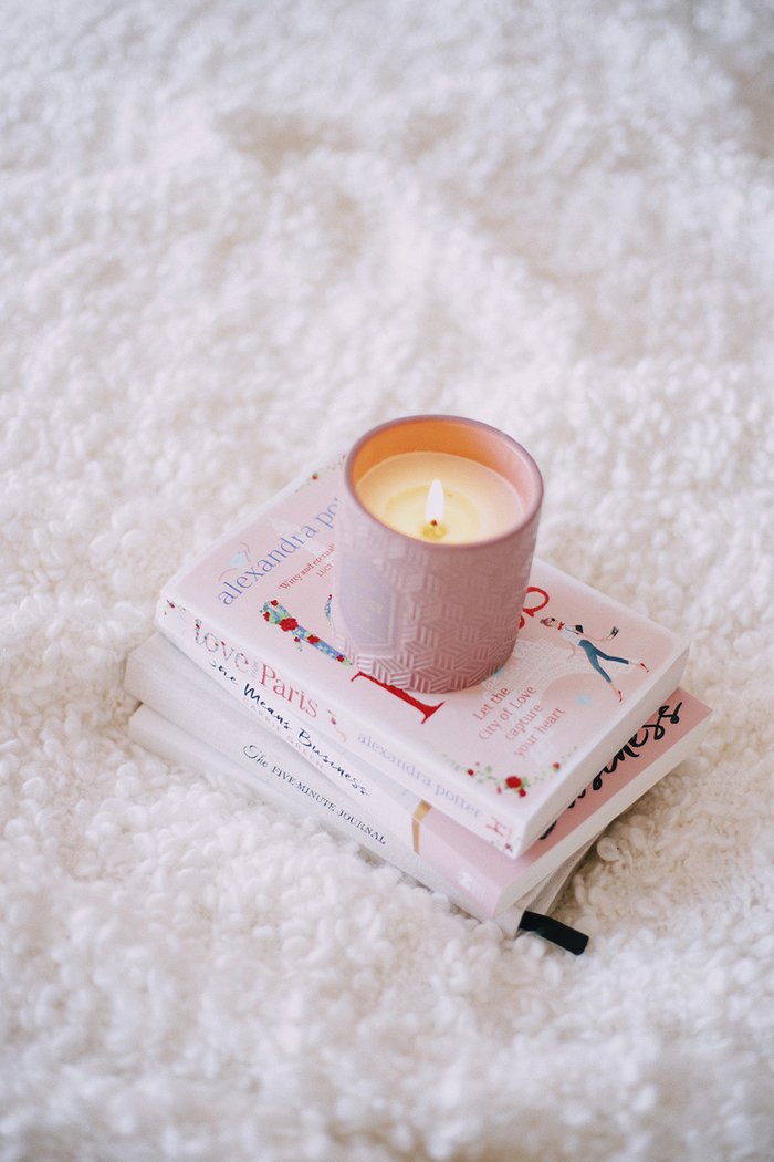 cozy days books lying on a soft bed covered with white blanket with a cozy pink candle on them