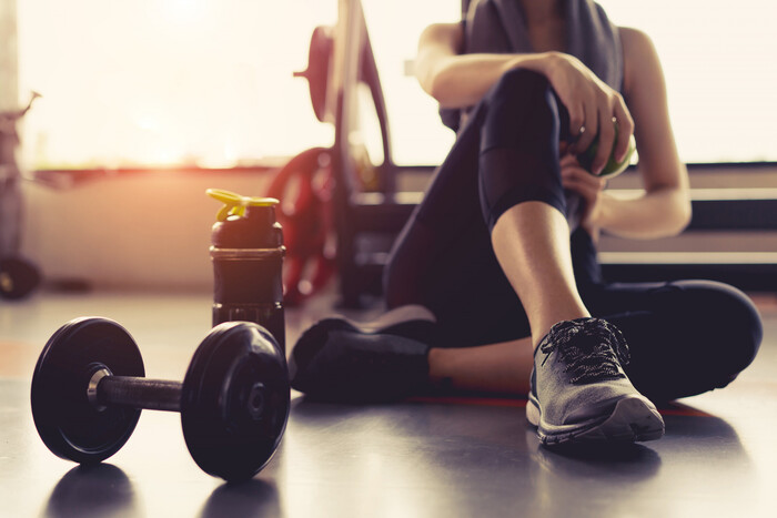 woman sitting in on the gym floor with her water bottle and weights sun shining in the background