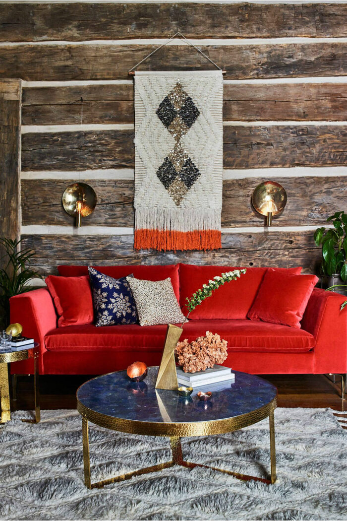 fall colors modern living room in jewel colors red couch blue and gold table and a rug hanging from a wooden wall