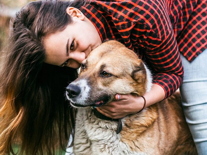 girl with a long hair and checkered red and black shirt and jeans kissing a large dog