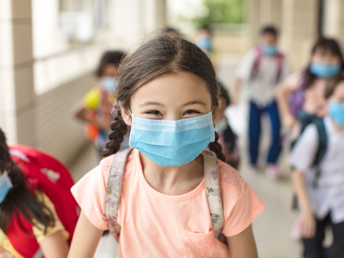 little girl in school with her hair braided with a blue mask on her face