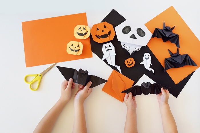 children playing a white table with different colors of paper cutting out bat ghost and pumpkin shapes