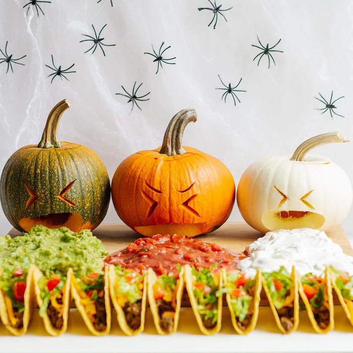 halloween pumpkin tacos with different sauces on a white cloth background with black spiders on