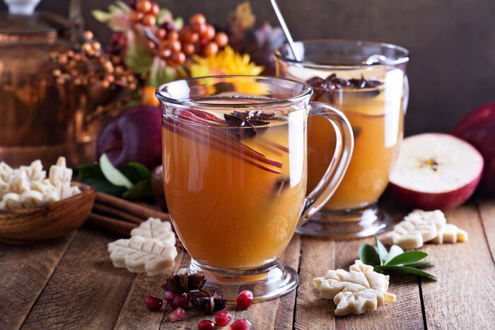 hot drinks two glasses on a wooden table with an orange tea inside garnished with spices fall decor in the background