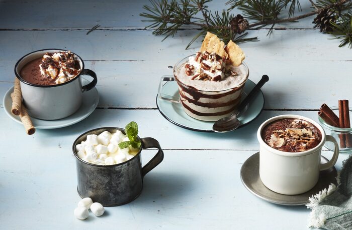 hot fall drinks in cute cups with different decorations on a light blue table 