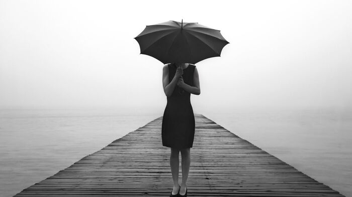 woman in a black dress standing on a peer in the rain holding a large black umbrella
