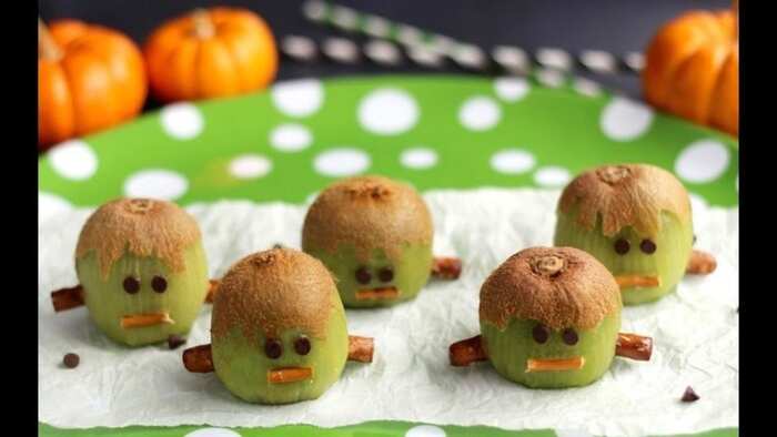 kiwi gohosts monsters halloween snack on a white paper napkin and a green dotted plate with orange pumpkins in the background