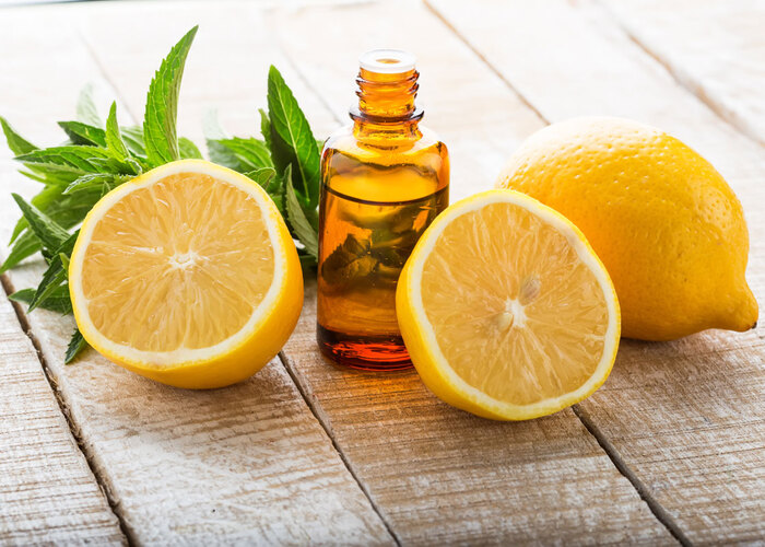 lemon essential oil in a brown bottle with sliced lemons around on a wooden table with peppermint leaves