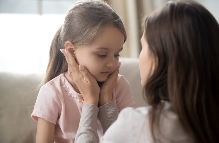 mom with a long dark hair holding the face of a little girl in pink and looking at her