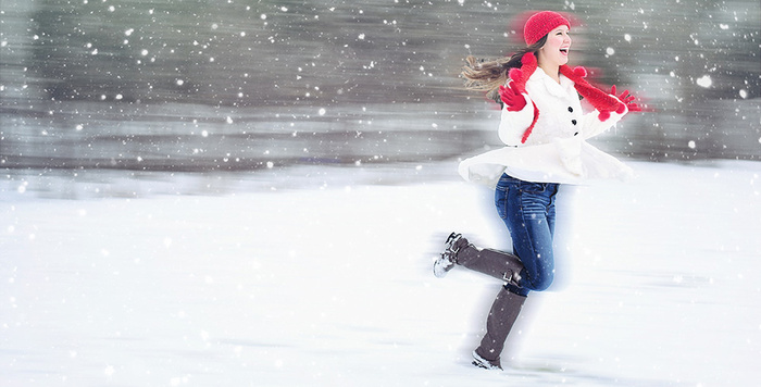 woman in jeans white coat red hat red gloves and scarf running outside in the snow smiling