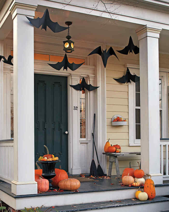 paper bats hanging from the ceiling on a porch with pumpkins and other decorations