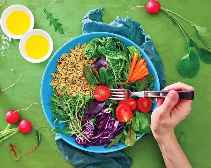 person eating a large bowl of salad on a green table with dressings in white bowls on the side