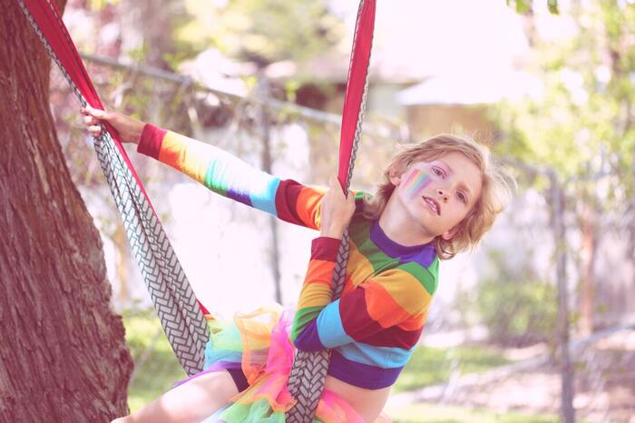 blond child in colorful shirt playing with a hammock outdoors on a tree