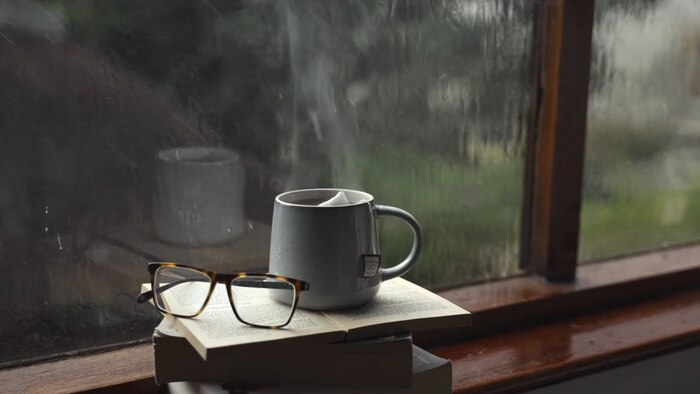 rainy day through the window with several books a pair of glasses and a large white mug with steaming tea