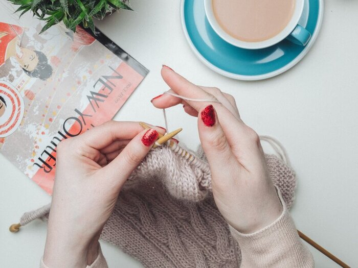 rainy days at home woman sitting on a table knitting with a blue mug with coffee in front of her and some magazines