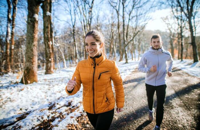 seasonal body changes couple jogging in the forest in winter with their jackets on 