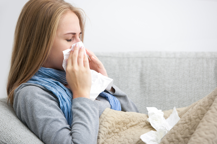 seasonal body changes blond woman lying on a couch with a blanket on wiping her nose with a tissue