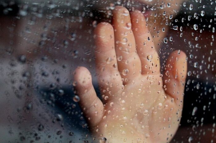 childs hand touching a window with rain drops on it from the inside