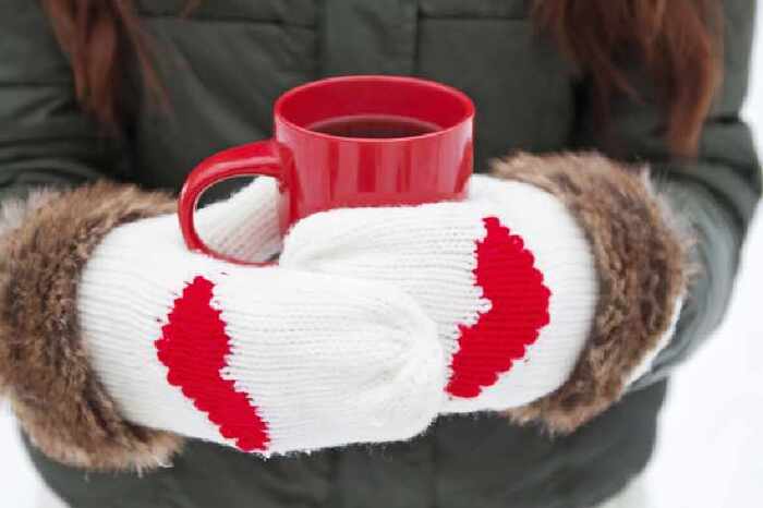 woman with white gloves with red hearts on them and a thick jacket drinking hot tea from a red mug