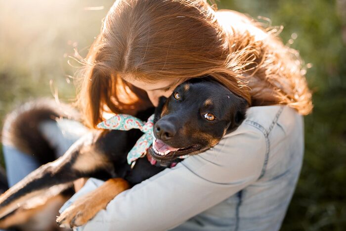 woman with long hair hugging a black dog with a scarf outside