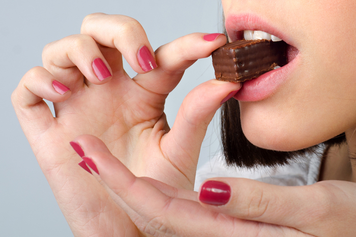 woman with nail polish on bringing a chocolate candy to her lips