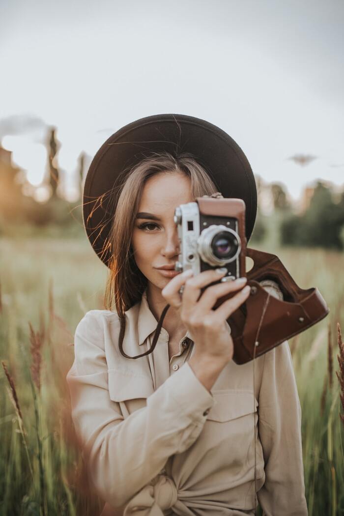 woman dressed in beige with a brown hat in the middle of a field with a camera taking pictures