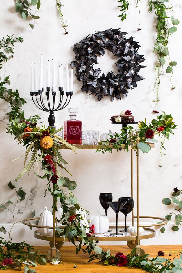 Black halloween wreath on a white wall with living plants and flower arrangements around