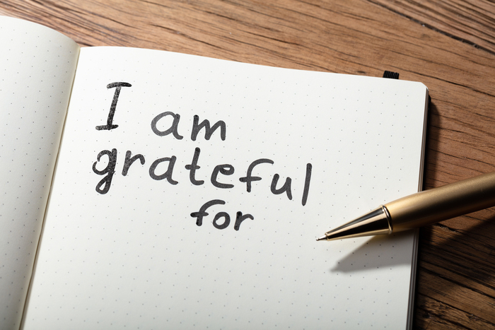 notebook with a message and a pen on a wooden table surface saying I am grateful