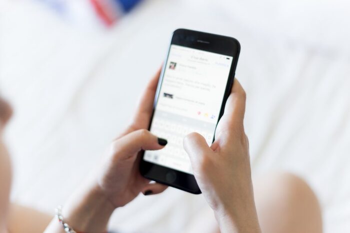 woman holding her black mobile phone looking at the screen and typing