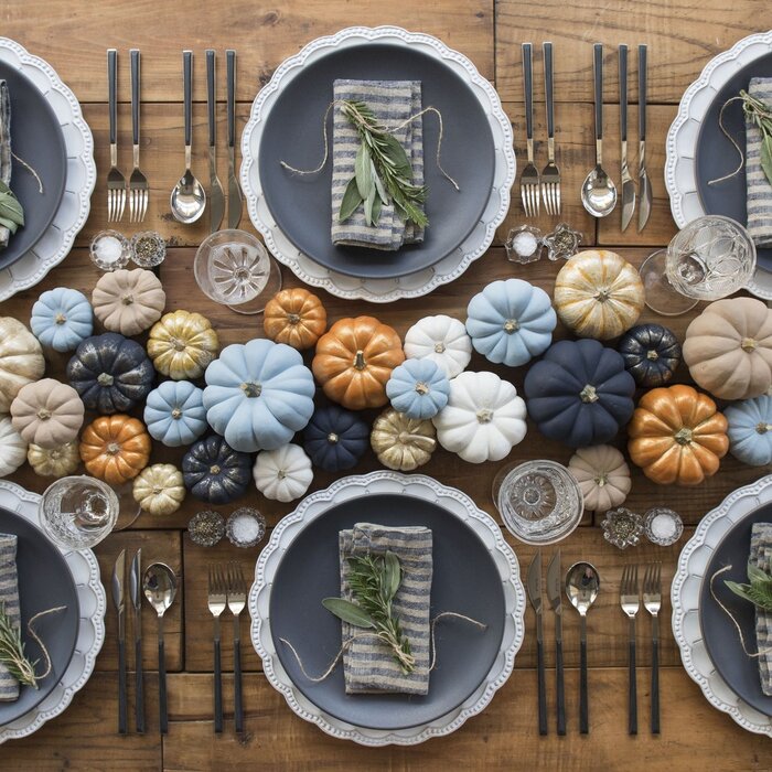 colorful pumpkins on a light wooden table with grey plates and green accents