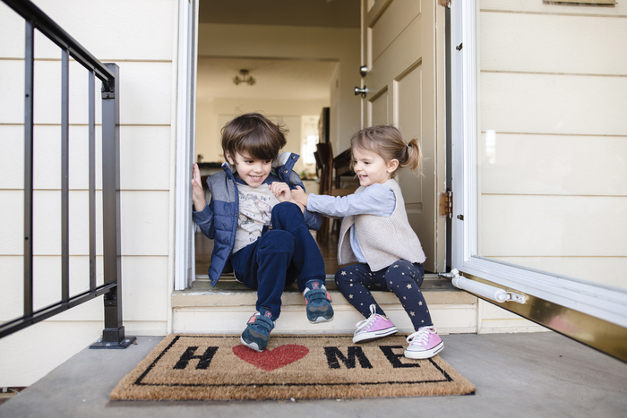 little boy and girl sitting at the door of a home playing and laughing