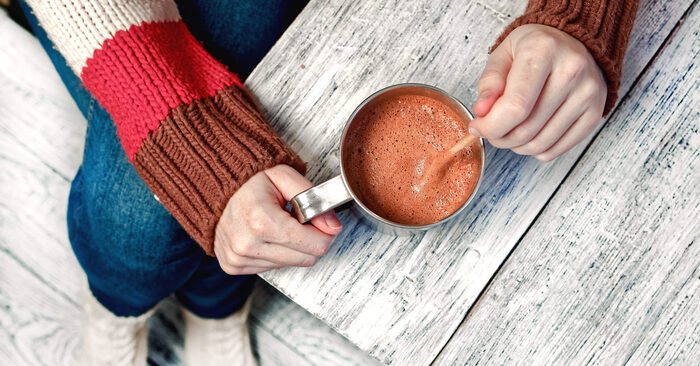 enjoying hot beverage woman in jeans and sweater sitting at a wooden table with a cup of hot cocoa 