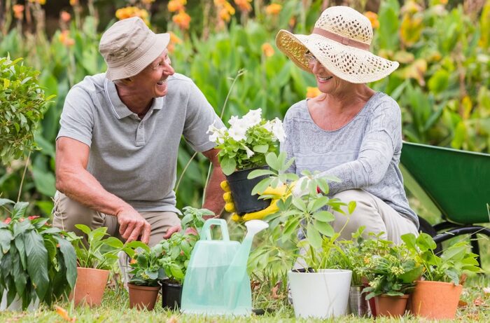 adult man and woman sitting in their garden with hats on smiling and working together