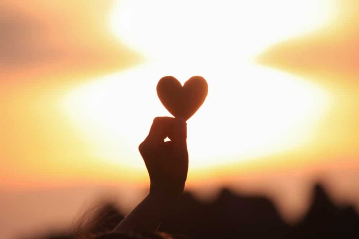 gratitude hand holding a little heart shape against the sunset
