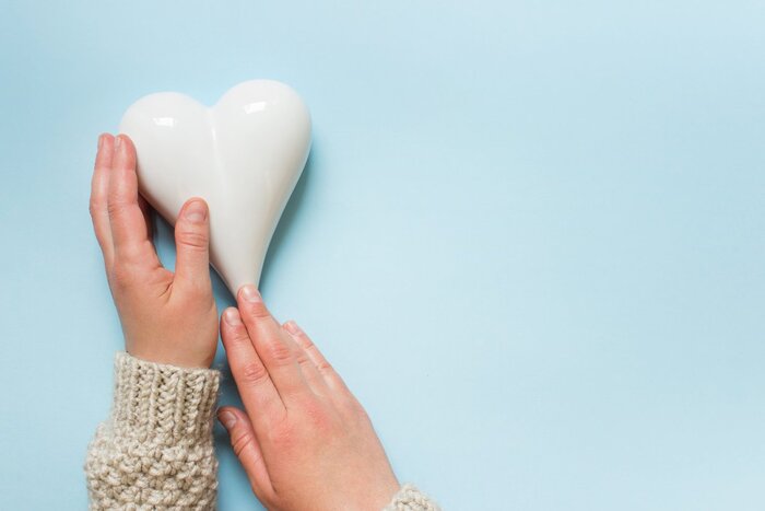 two hands holding a ceramic heart shape on a blue background