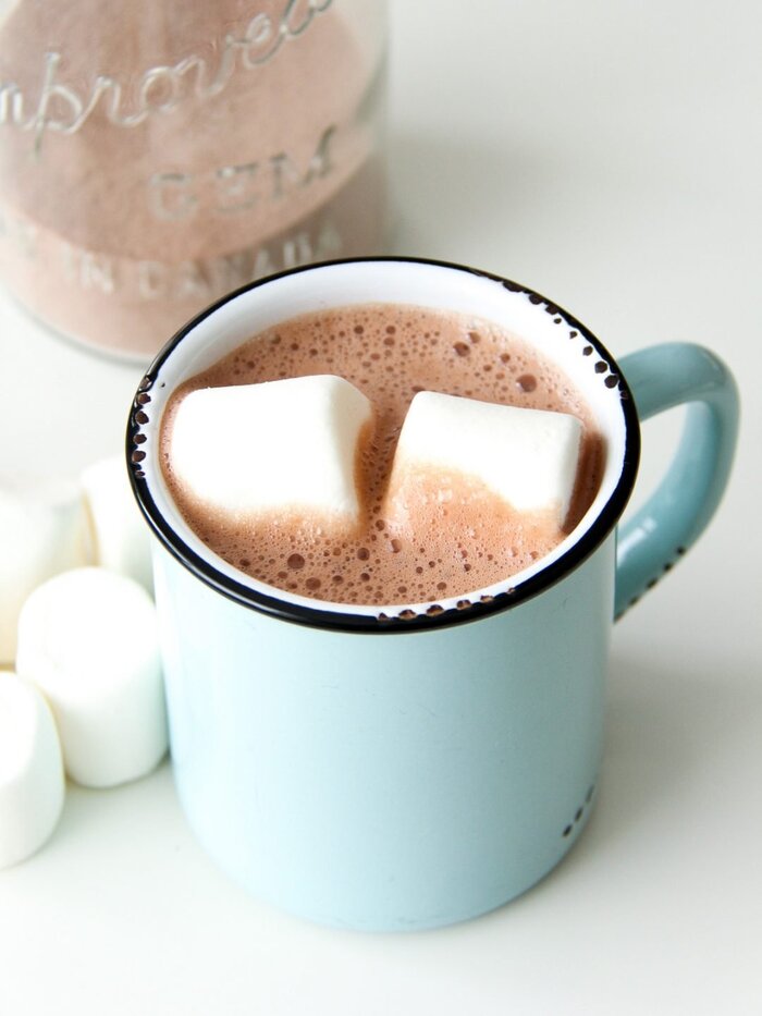 preparing hot cocoa in a light blue mug with two white marshmellows floating inside