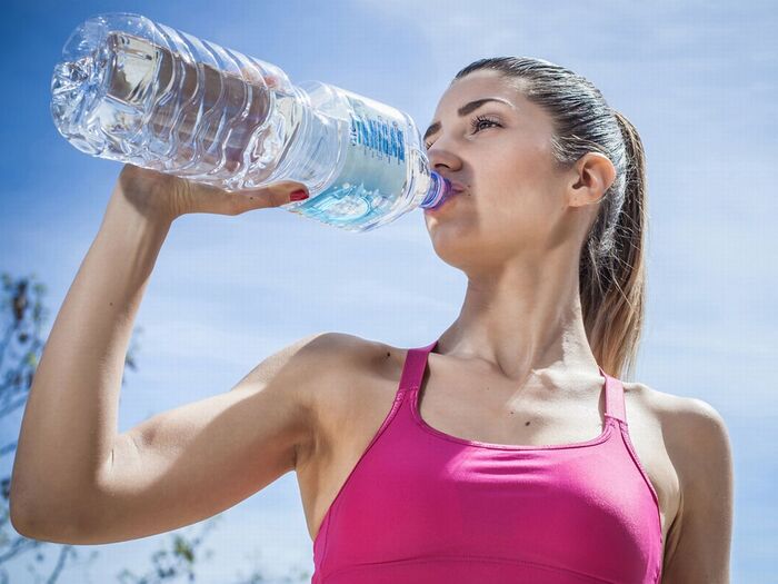 woman in a pink sporty top and a pony tail working out outdoors drinking water from a large plastic bottle